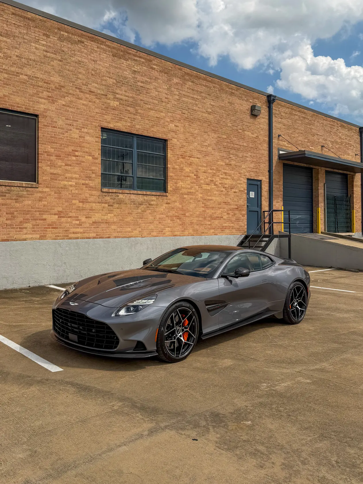 Gray 2025 Aston Martin Vanquish parked outside a brick warehouse building