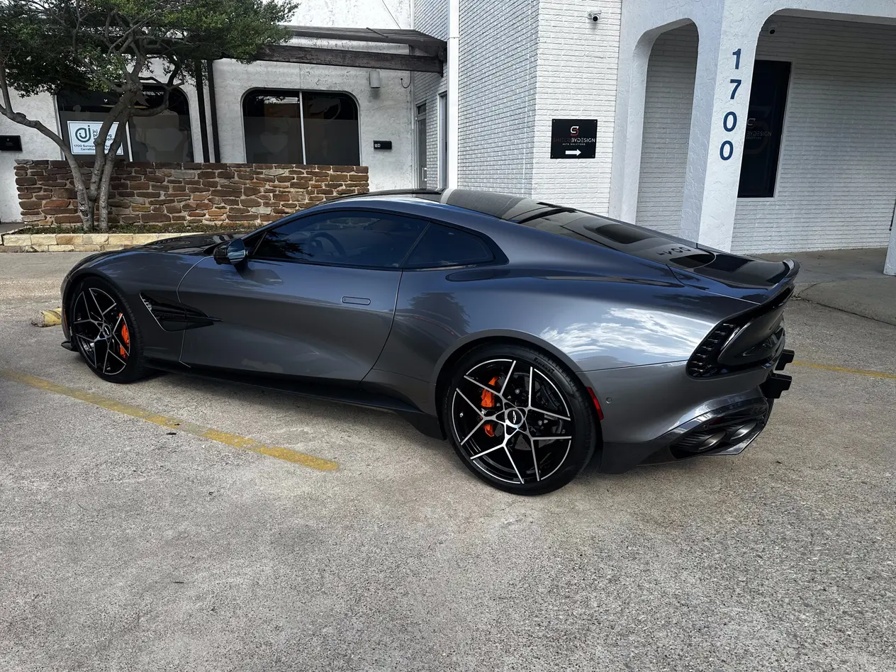 Dark gray Aston Martin coupe with tinted windows parked outside a shop