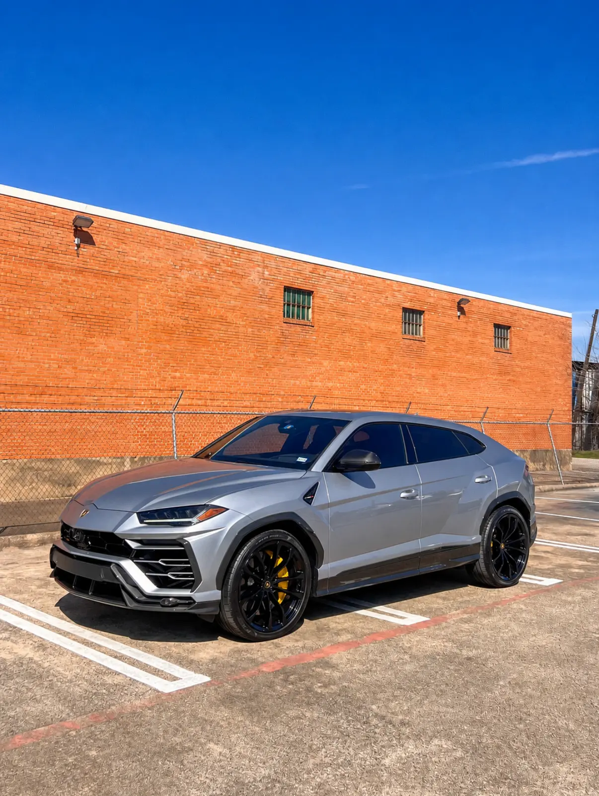 Silver Lamborghini Urus parked outside a brick warehouse building